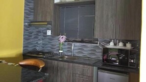 A compact kitchen with dark wood cabinets, a built-in microwave, and a small refrigerator. - DreamWest Living Guesthouse  (Krugersdorp)