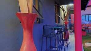 A covered outdoor area with a tiled floor, a large red vase, and several plastic chairs. - DreamWest Living Guesthouse  (Krugersdorp)