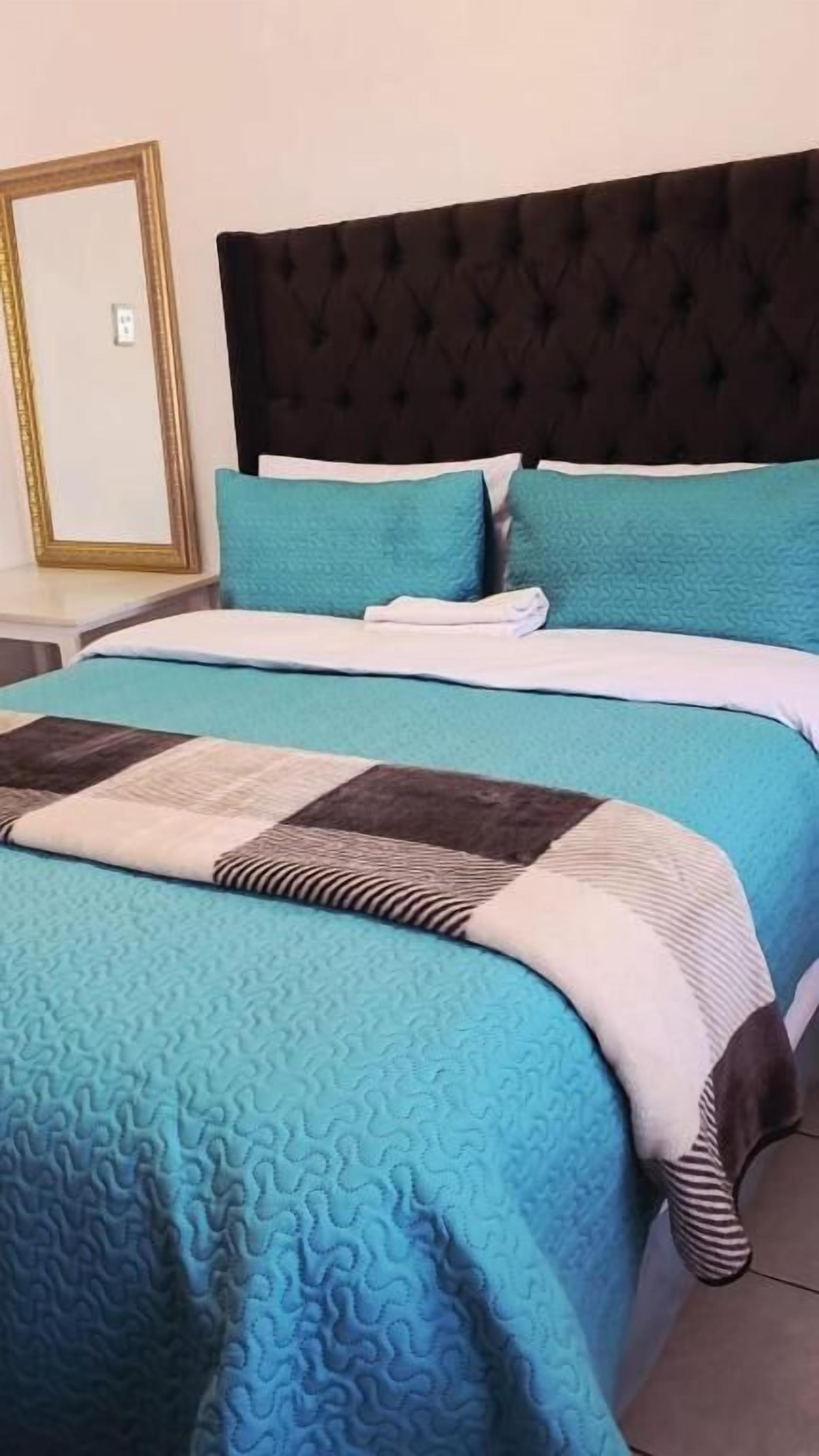 A bed with a blue quilt and a brown and white quilted blanket.
