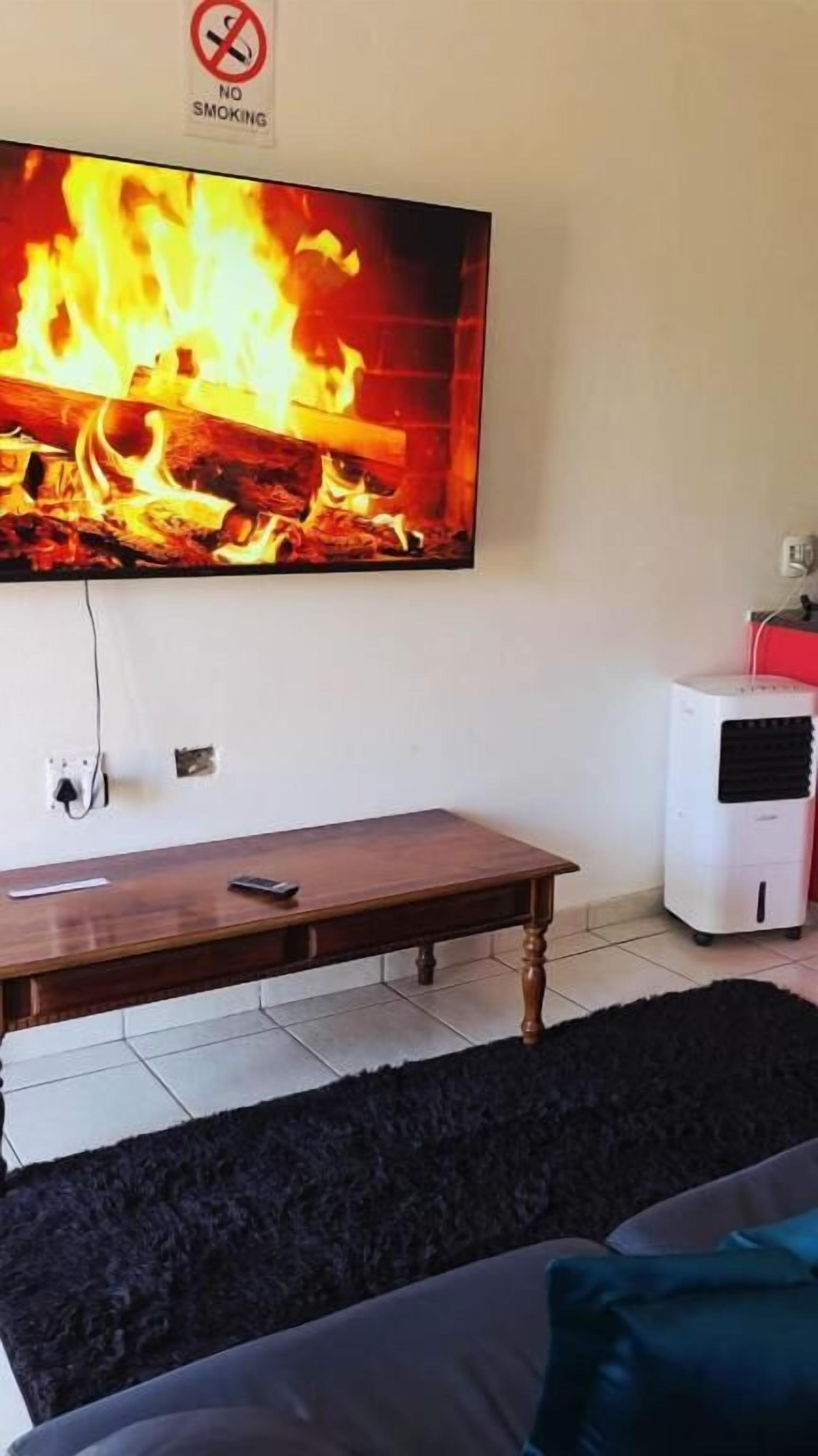 Un salón con televisor mostrando fuego, una mesa de madera, un tapete negro y mullido, y un aire acondicionado blanco.