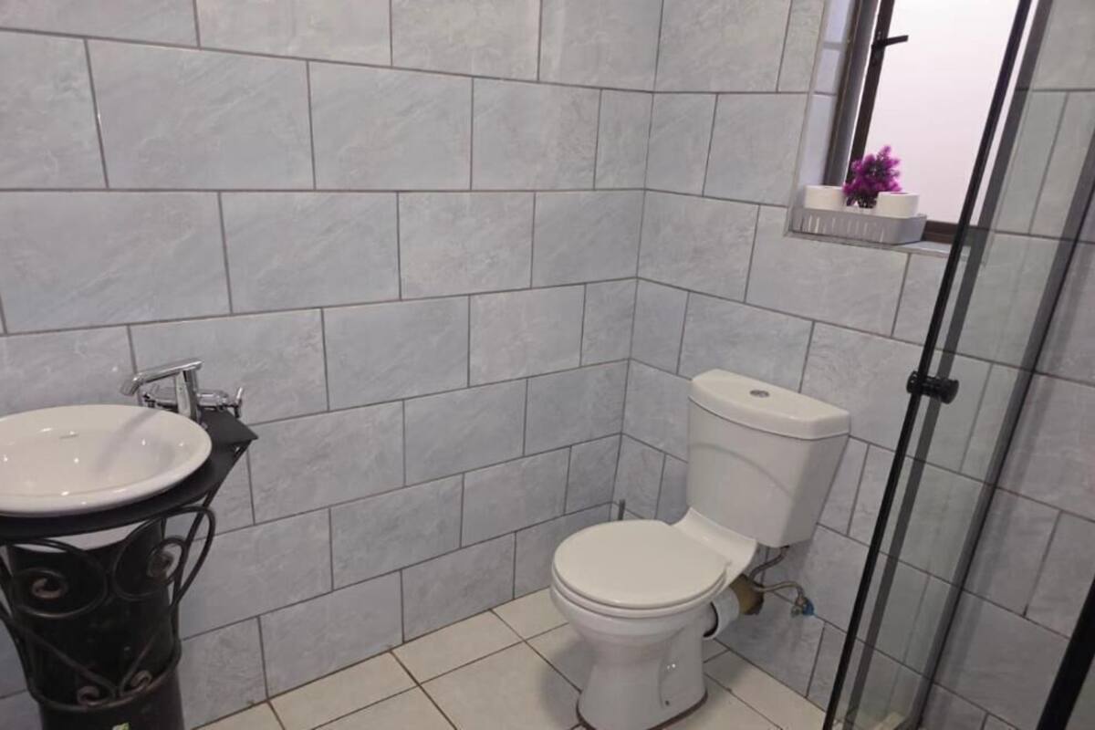 Ein Badezimmer mit Toilette, Waschbecken und einer kleinen Ablage mit einer violetten Blume.