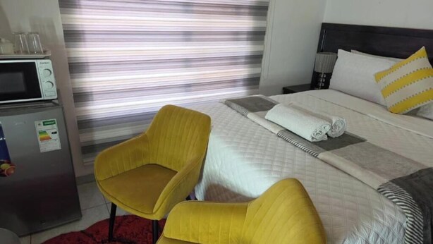 A hotel room with a bed, a yellow armchair, a microwave, and a refrigerator. - DreamWest Living Guesthouse  (Krugersdorp)