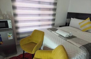 Una camera d'albergo con un letto, una poltrona gialla, un forno a microonde e un frigorifero.