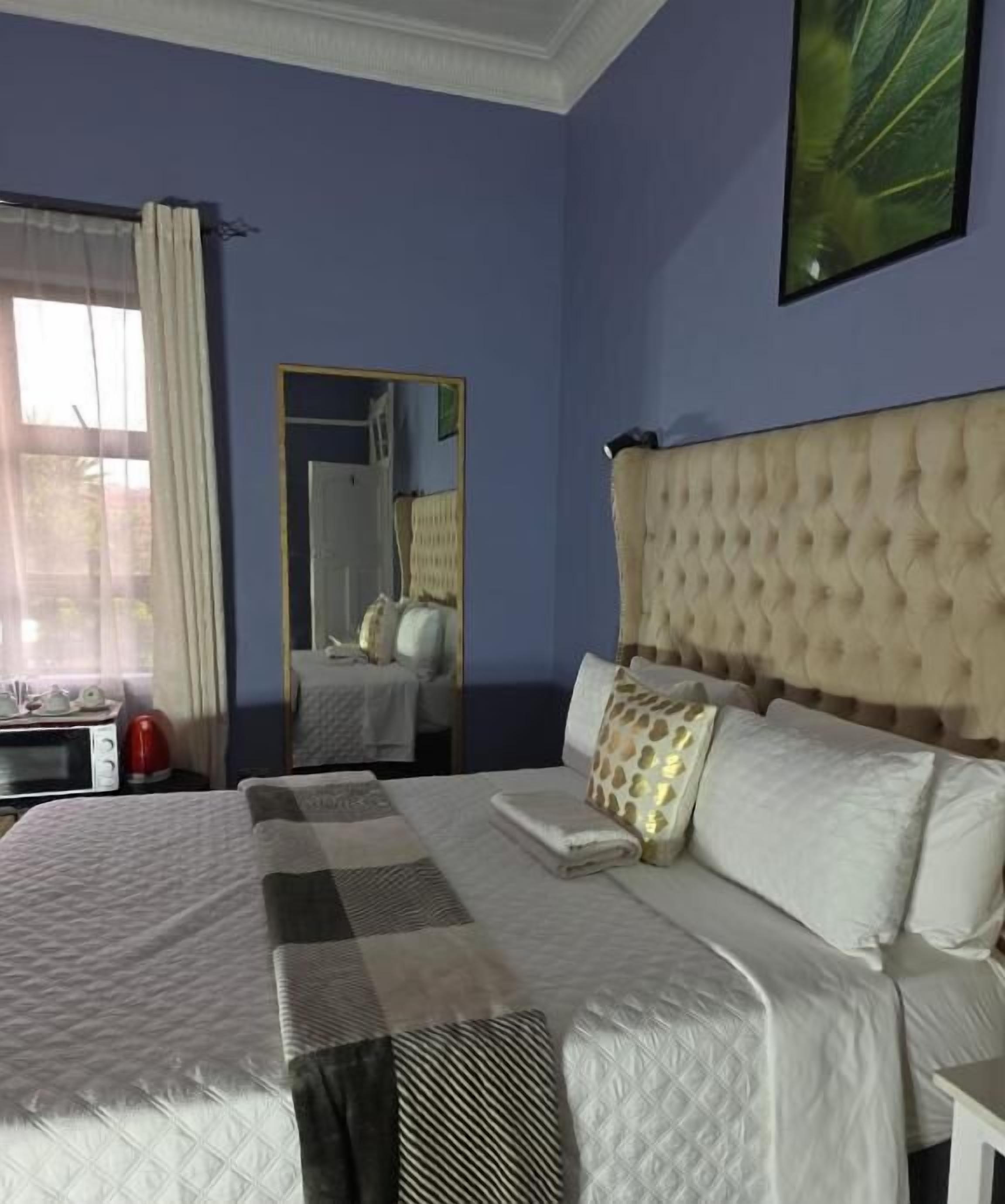 A hotel room with a large bed, a mirror, a window with curtains, and a microwave on the side table.