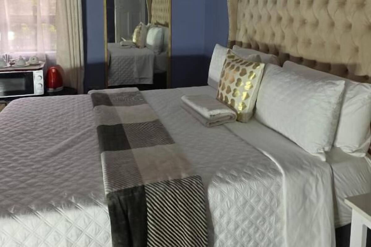Ein Hotelzimmer mit einem großen Bett, einem Spiegel, einem Fenster mit Vorhängen und einer Mikrowelle auf dem Nachttisch.