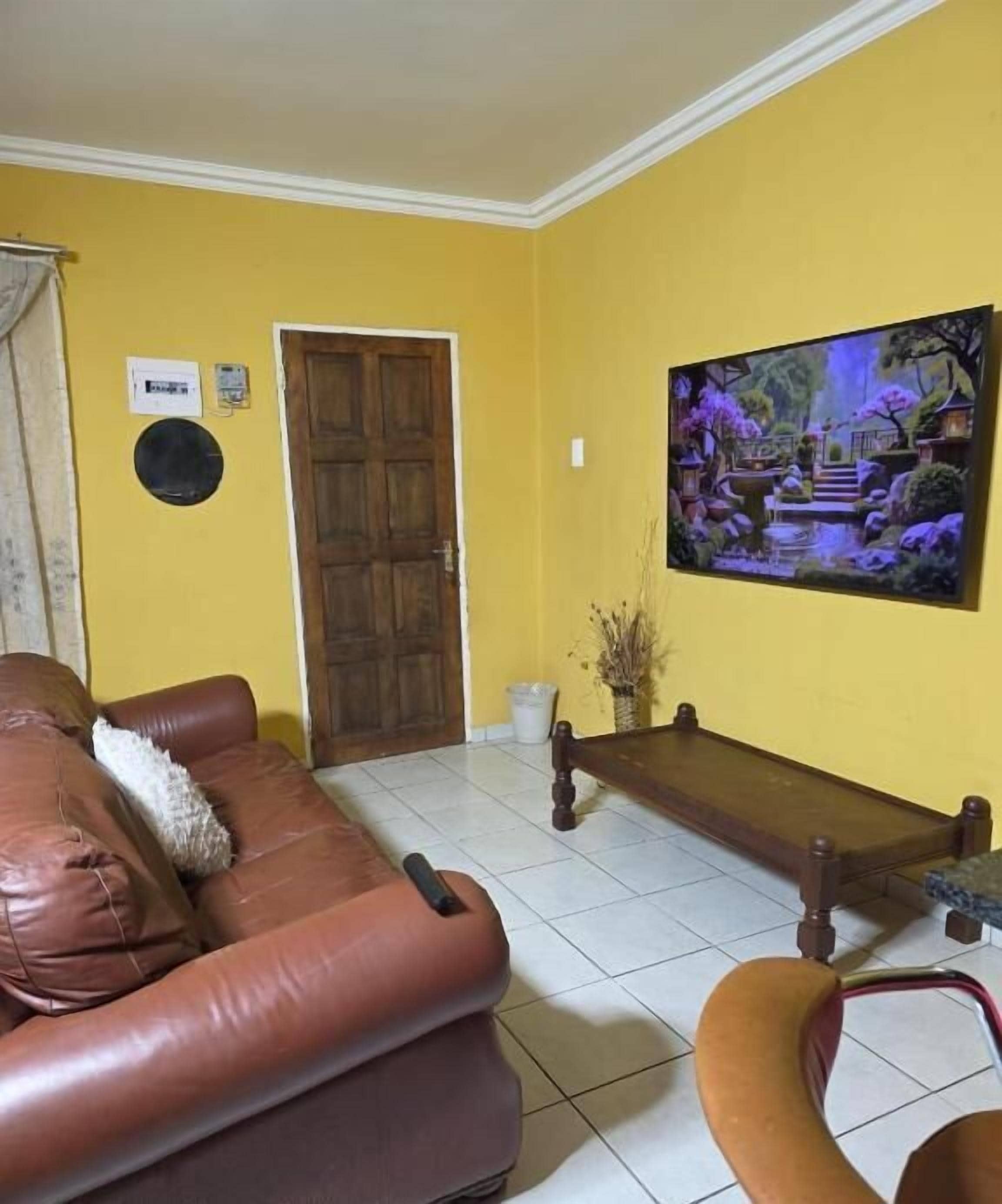 Uma sala de estar com um sofá de couro marrom, um banco de madeira e um quadro com uma cena de jardim na parede.