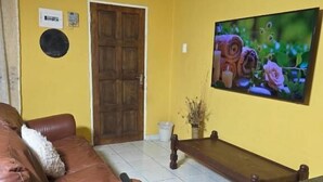 A living room with a brown leather sofa, a wooden bench, and a TV on the wall. - DreamWest Living Guesthouse  (Krugersdorp)