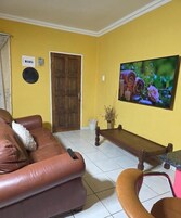 Una sala de estar con un sofá de cuero marrón, un banco de madera y un televisor en la pared.
