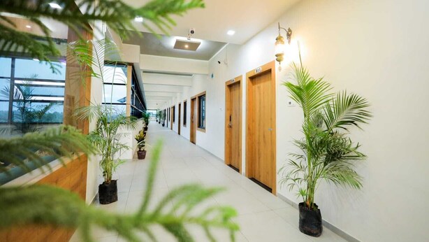 Un pasillo moderno de hotel con puertas de madera, plantas en macetas y una escalera que sube a un nivel superior.
