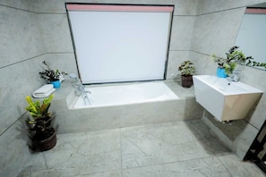 A bathroom with a bathtub, a sink, and two potted plants.