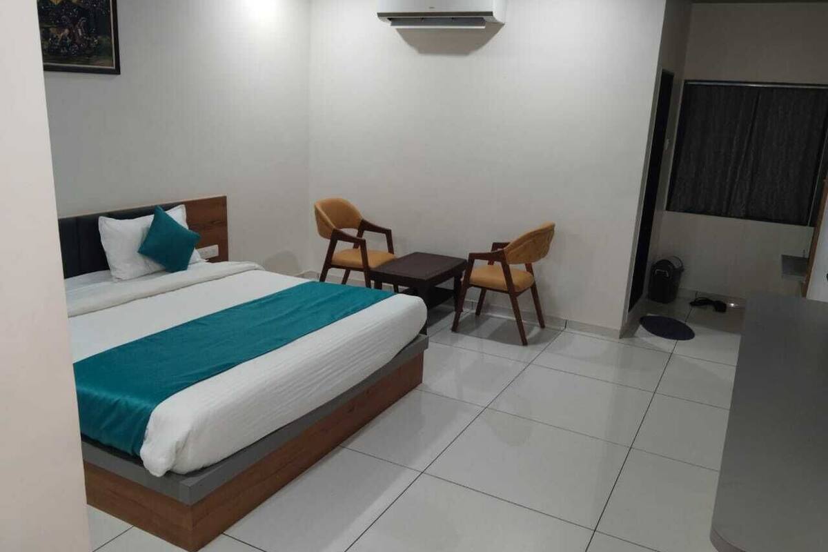 A hotel room with a bed, two chairs, a small table, and a trash bin.