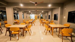 Un comedor amplio con varias mesas y sillas, ventiladores de techo e iluminación empotrada.