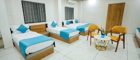 A hotel room with three beds, a wooden wardrobe, a small round table with chairs, and ceiling fans.