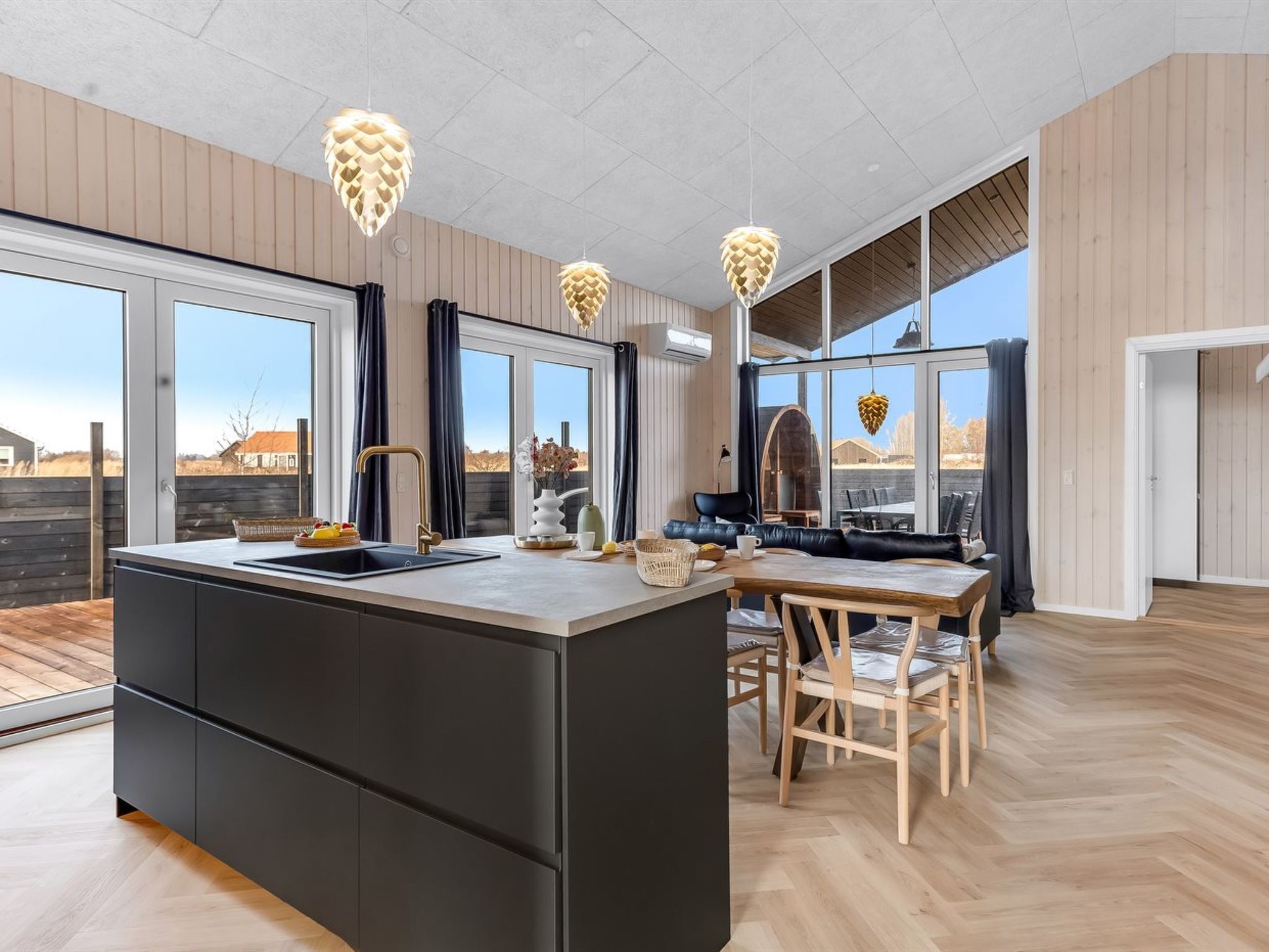 Et moderne køkken med en central ø, store vinduer og et spiseområde med et træbord og stole.