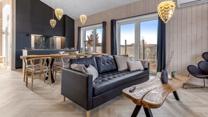Un salon moderne avec un canapé en cuir noir, une table à manger en bois et des luminaires suspendus.