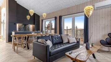 A modern living room with a black leather sofa, wooden dining table, and pendant lights.