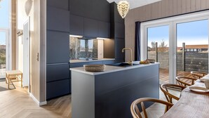 Une cuisine moderne dotée d’un îlot central, de meubles de rangement aux couleurs sombres et d’une grande fenêtre offrant une vue sur l’extérieur.