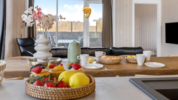 Un coin repas avec une table mise pour le petit-déjeuner, comprenant un panier de fruits, des tasses à café et une vue sur l’extérieur.