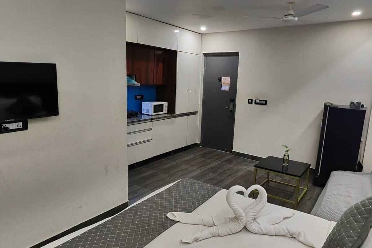 Habitación de hotel con cama, televisión montada en la pared, kitchenette con microondas y una puerta con un cartel.