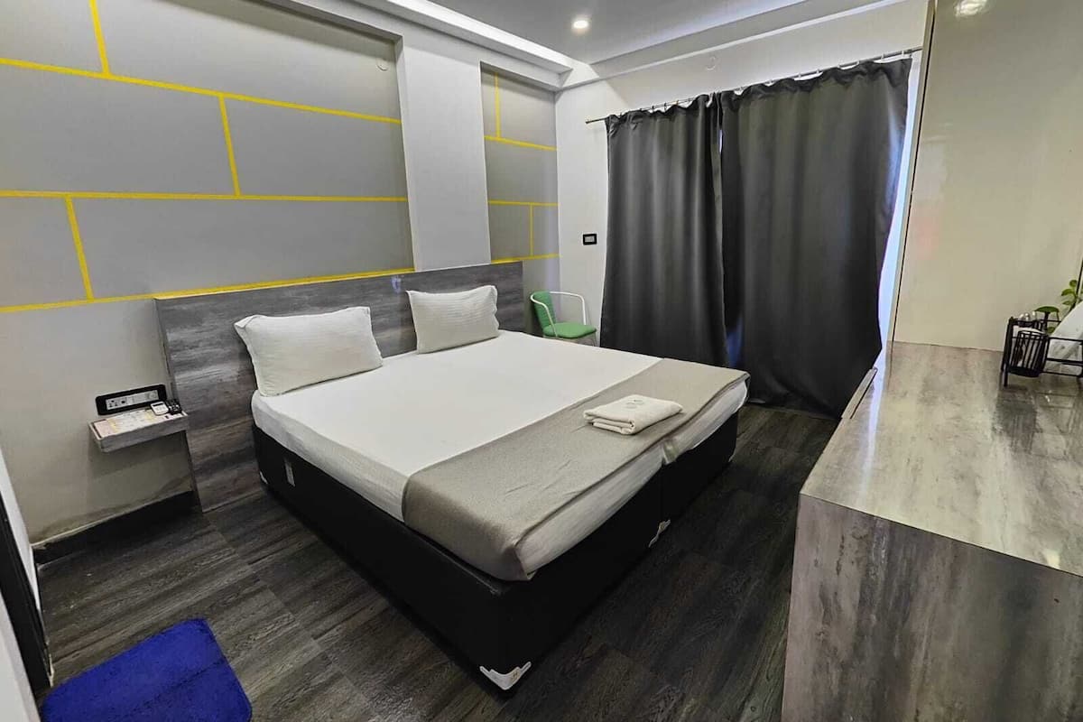 Una habitación de hotel moderna con una cama grande, una mesita de noche, un escritorio pequeño y una ventana con cortinas.