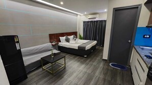 Habitación de hotel compacta con cama, sofá, una mesita, kitchenette y baño.