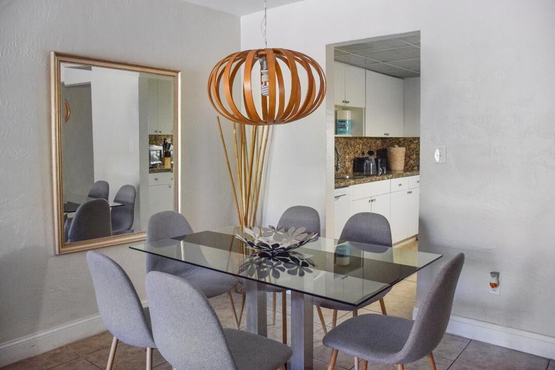 A dining area with a glass table, grey chairs, a decorative centerpiece, and a modern pendant light.