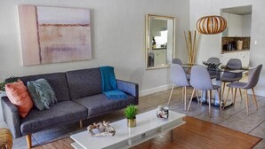 A modern living room with a gray sofa, a coffee table, and a dining area with chairs and a table. - Relaxed 2BR Coastal Haven with Pool, Minutes from the Beach! - (Key Biscayne)