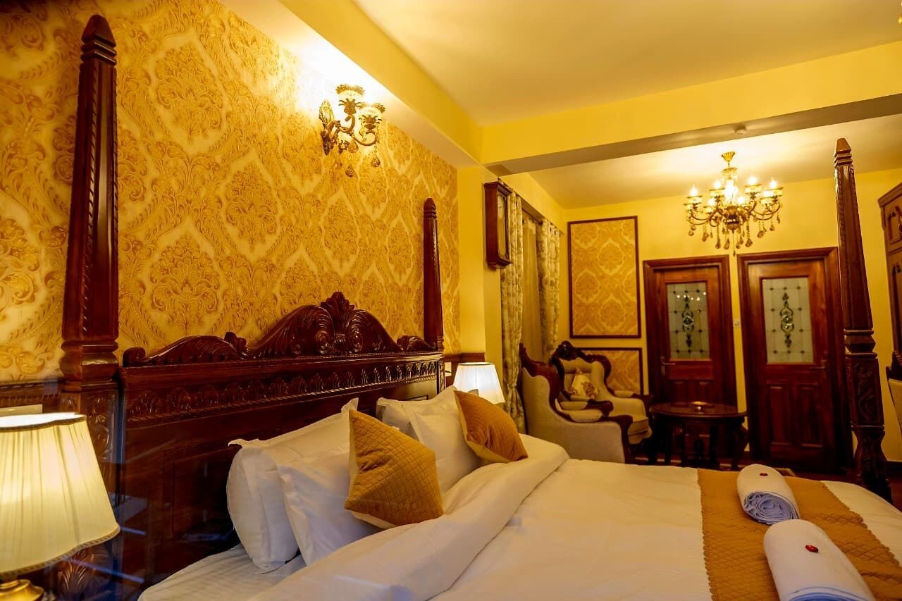 A hotel room with a large bed, ornate headboard, and a chandelier.