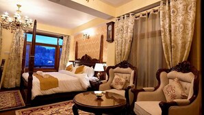 A hotel room with a large bed, two armchairs, a round coffee table, and a chandelier. - The Himalayan Heritage (Shimla)