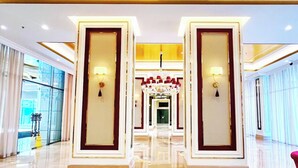 A hotel corridor with a reflective floor, large doors with wall sconces, and a chandelier. - Trans Park Apartment Cibubur by Housleep (Depok)