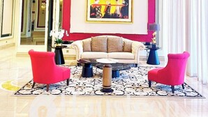 A modern lobby with a beige sofa, red armchairs, and a large abstract painting on the wall. - Trans Park Apartment Cibubur by Housleep (Depok)