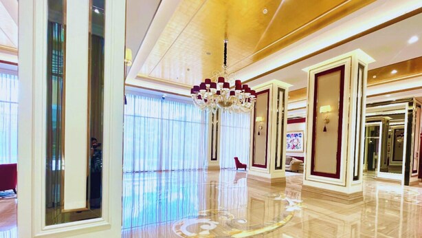 A spacious lobby with a polished floor, a grand chandelier, and a red accent wall. - Trans Park Apartment Cibubur by Housleep (Depok)