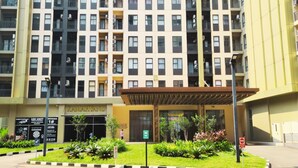 A multi-story residential building with a central entrance, a signboard, and a landscaped garden area. - Trans Park Apartment Cibubur by Housleep (Depok)