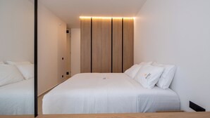Quarto moderno com cama grande, cabeceira de madeira e mesa de cabeceira.