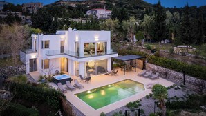 Uma casa moderna de dois andares com piscina, área de estar externa e um muro de pedra.