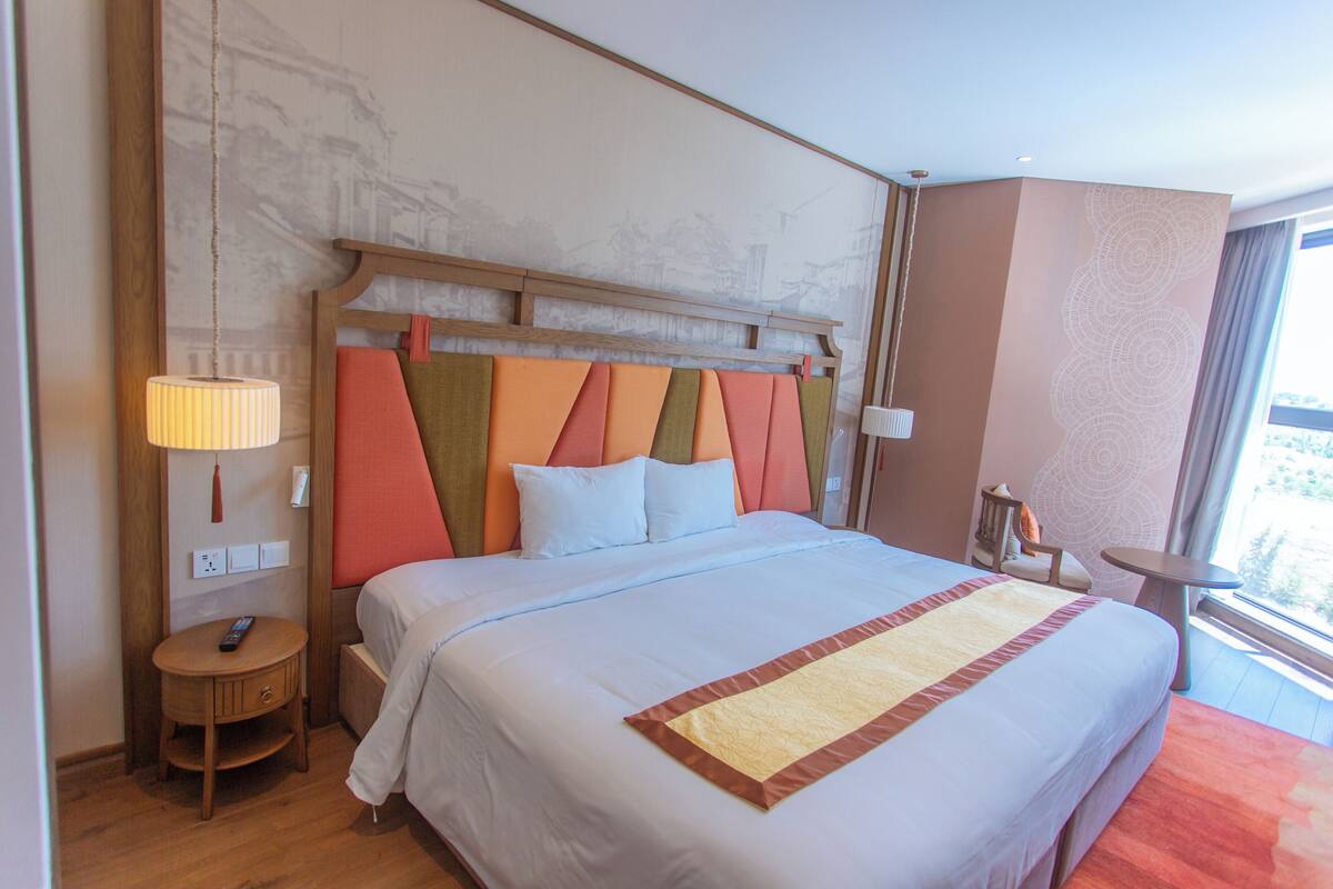 Een hotelkamer met een groot bed, nachtkastjes, een stoel en een raam met uitzicht.