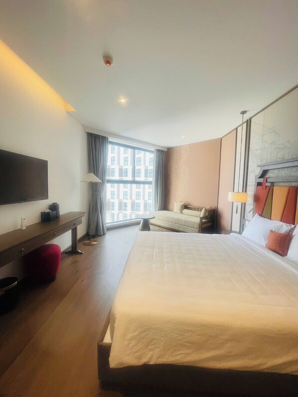 A hotel room with a large bed, a TV on a stand, a sofa, and a desk with a lamp.