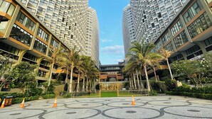 A modern urban plaza with tall residential buildings, palm trees, and a patterned pavement.