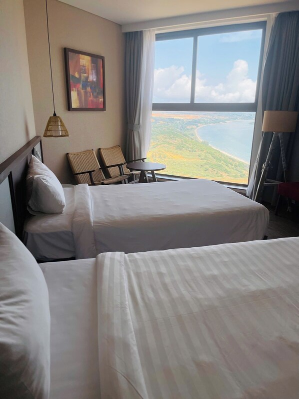 Une chambre d’hôtel avec deux lits, une table à manger et une vue sur un paysage côtier.