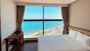 A hotel room with a large bed, a desk, and a view of the beach.