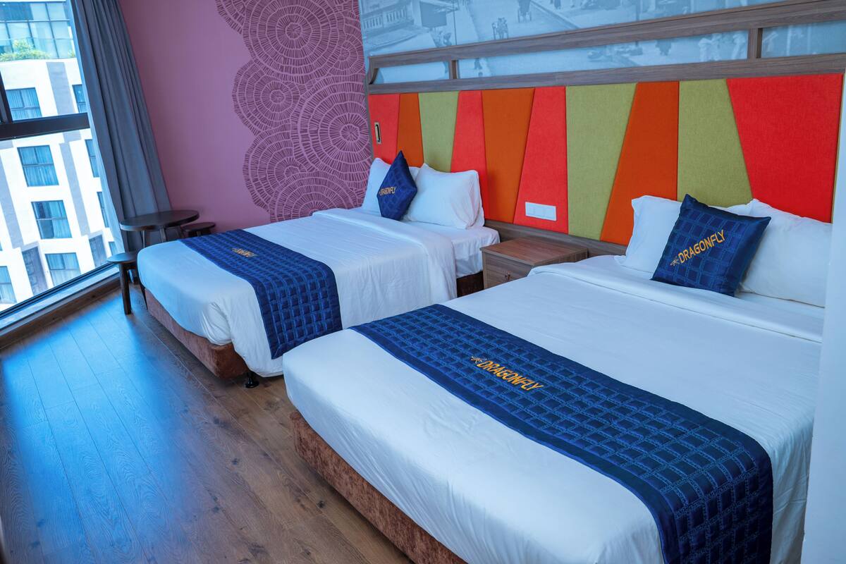 Een hotelkamer met twee bedden, een groot raam en een kleurrijk hoofdeinde.