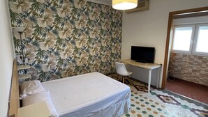 Un dormitorio con cama, escritorio, televisor y pared con estampado.