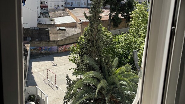 Vista desde una ventana sobre una zona residencial con edificios, un árbol y un campo deportivo.