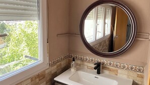 Un baño con ventana, lavamanos, espejo y salpicadero de azulejos.
