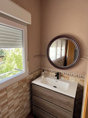 Ein Badezimmer mit Fenster, Waschbecken, Spiegel und Fliesenrückwand.