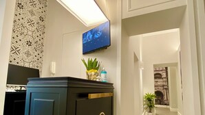 A hallway with a black cabinet featuring a gold emblem, a mounted TV, and a potted plant. - L'Infinito88 Charmant rooms (Naples)