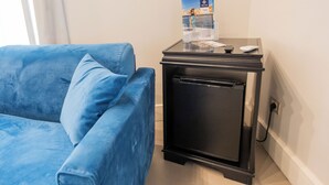 A room with a blue sofa, a small black refrigerator, and a table with a brochure. - L'Infinito88 Charmant rooms (Naples)