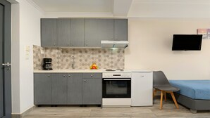 A compact kitchen with grey cabinets, a white stove, and a small dining area with a blue sofa. - Pnoe Beachside Studio (Georgioupoli)