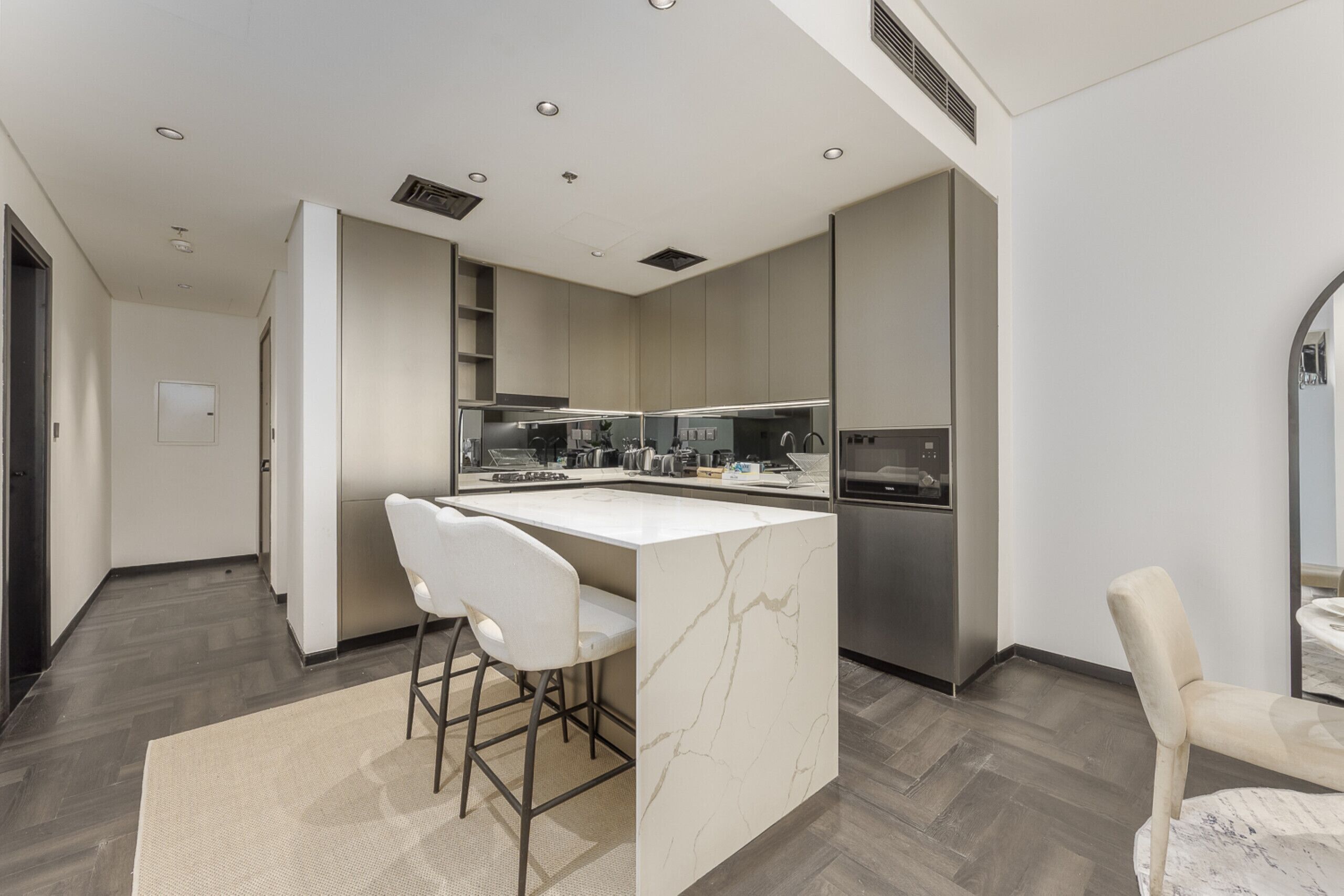 Een moderne keuken met een centraal eiland, barstoelen en roestvrijstalen apparatuur.