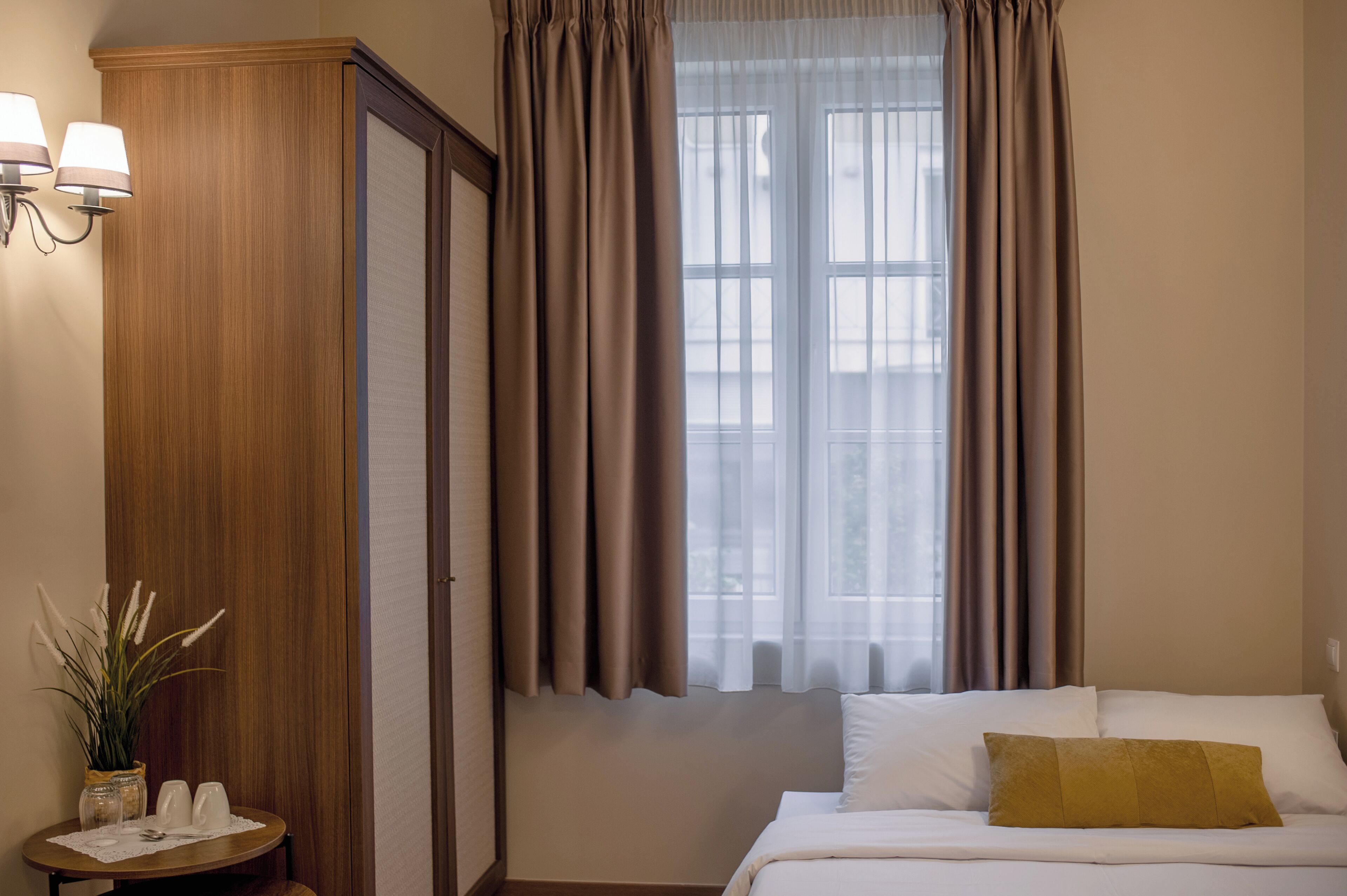 A hotel room with a bed, a nightstand, a lamp, a window with curtains, and a view of the outside.